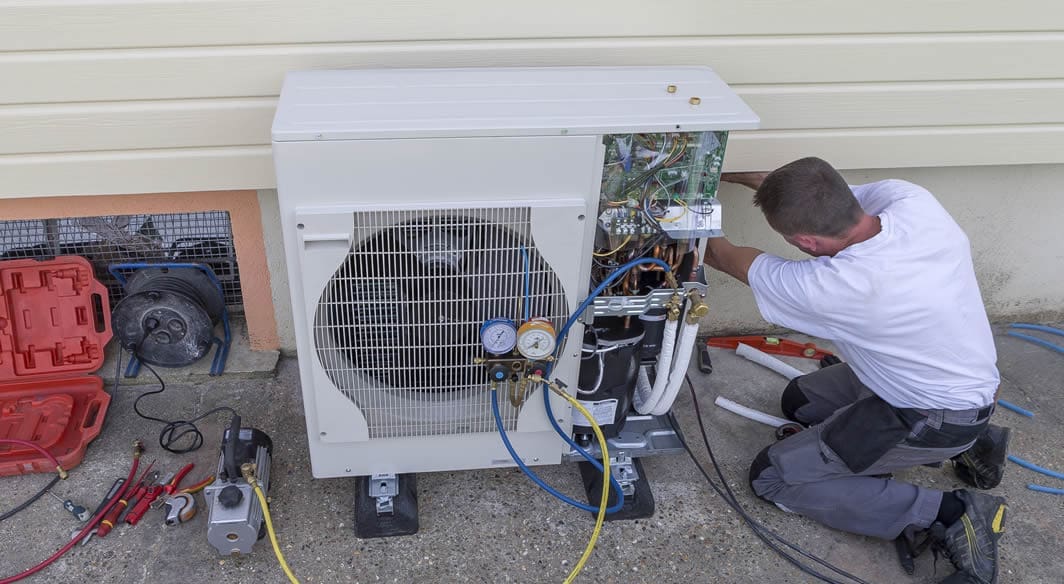 heating-contractor-working-1 Technician repairing outdoor HVAC unit.